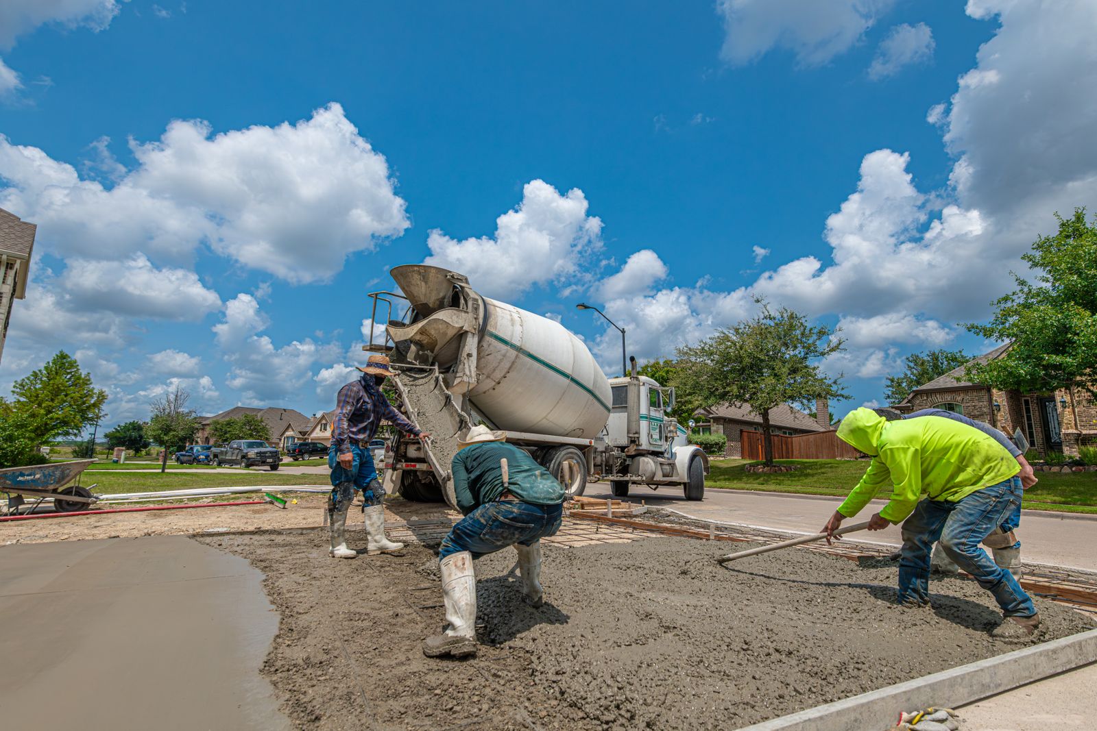 Concrete crew placing and finishing a driveway slab behind a mixer truck under a blue sky