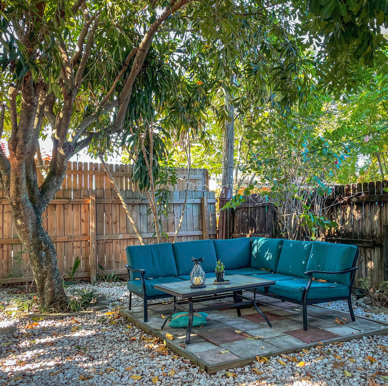 Concrete backyard patio with a teal outdoor sofa, a fence, and trees