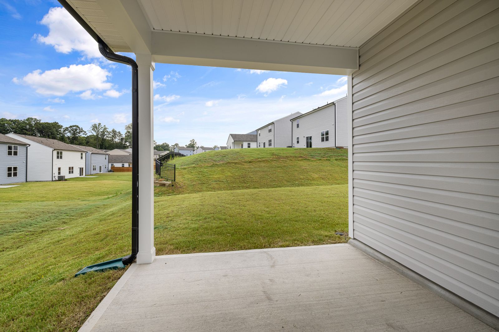 Covered concrete patio at the back of a suburban home looking out over a lawn
