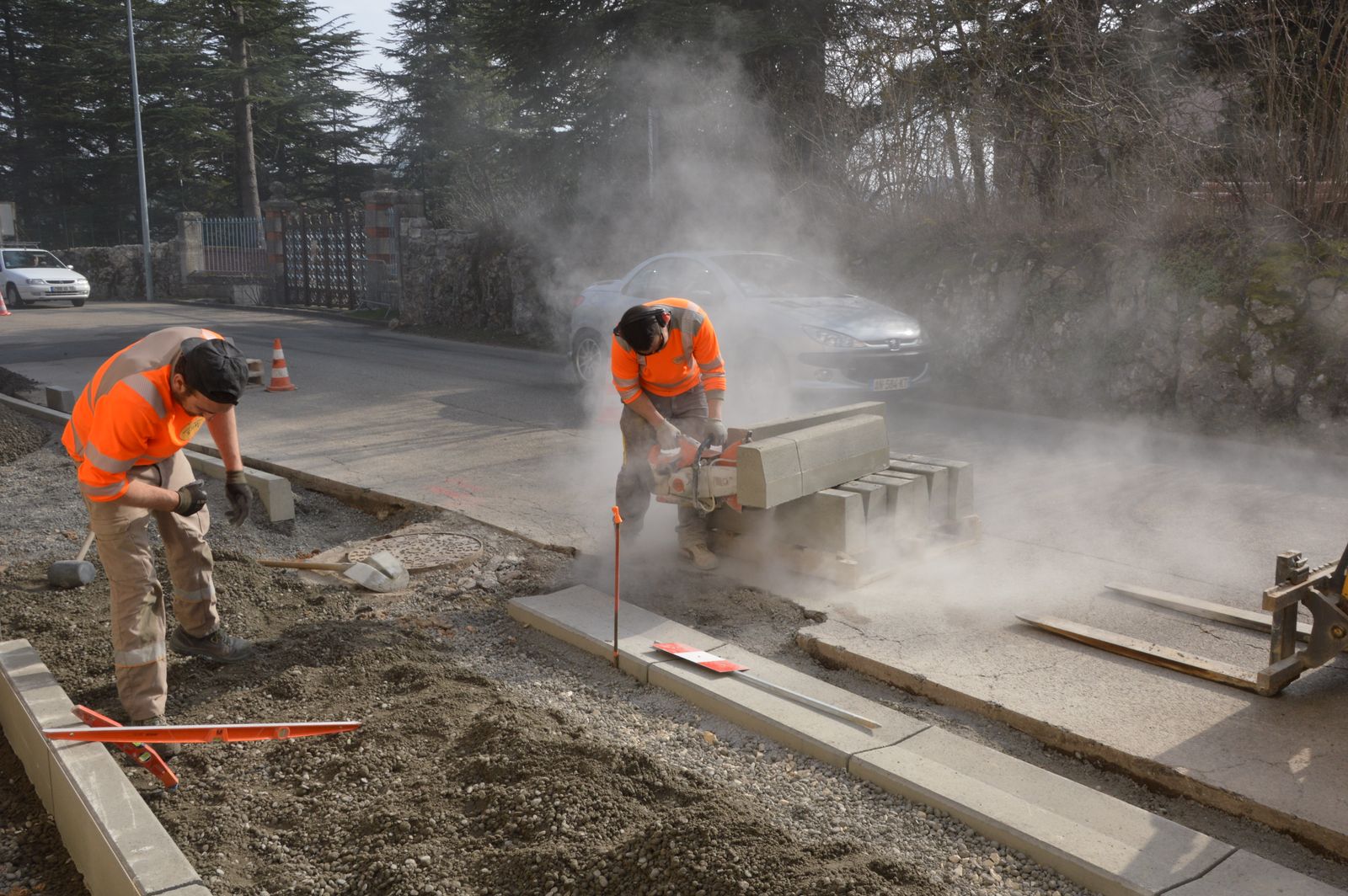 Worker in an orange hi-vis shirt cutting a concrete slab with a saw, with dust in the air